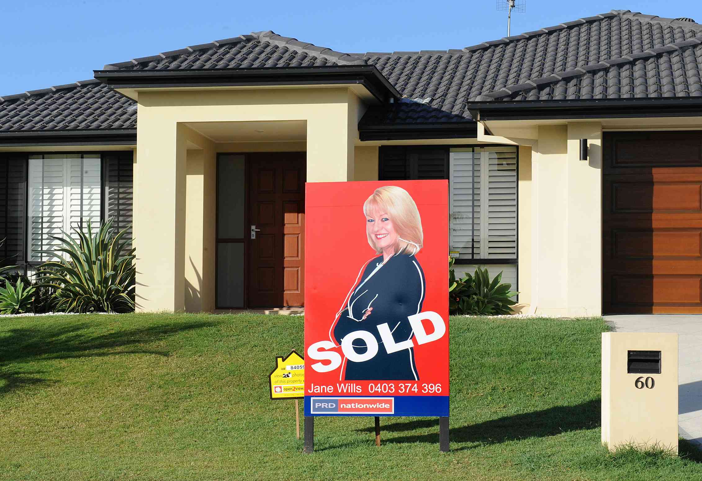 house with front lawn and sold sign depicting blonde woman