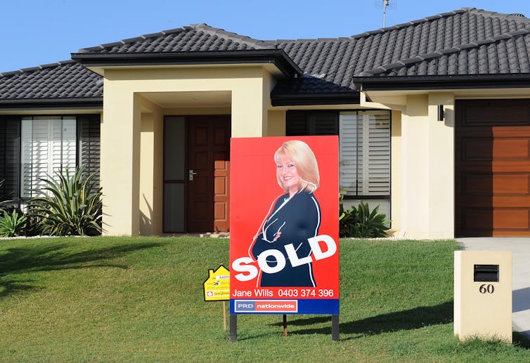 house with front lawn and sold sign depicting blonde woman