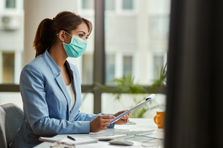 Woman in a mask works at a desk.
