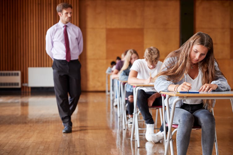 Invigilator walks among students sitting an exam