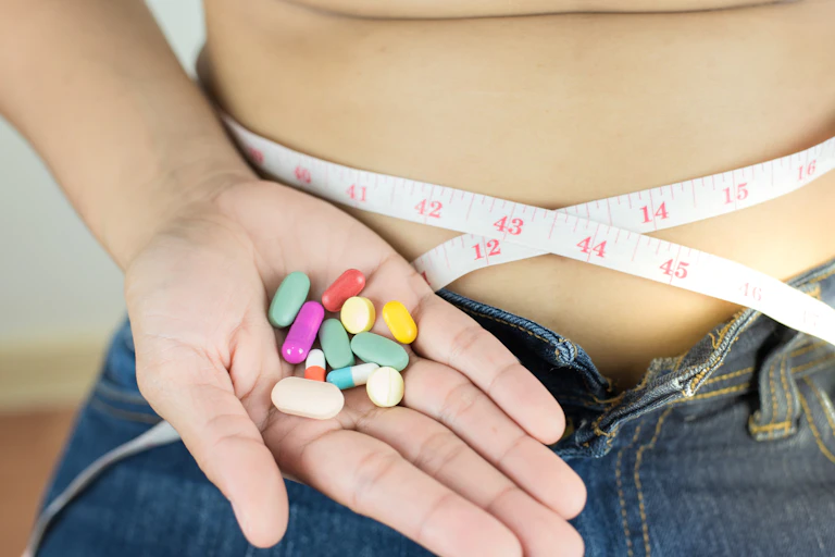 Tape measure around a waist and a hand full of coloured pills.