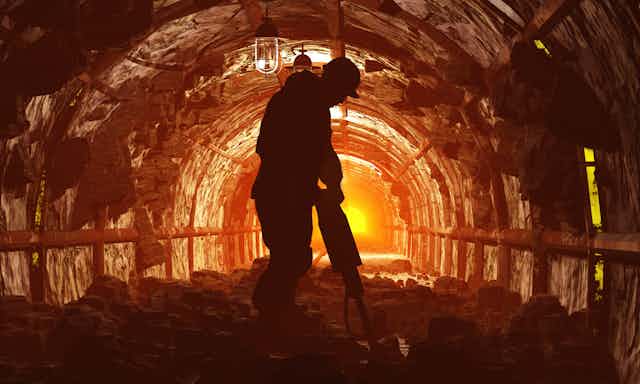 A silhouette of a person using a drill in a mining tunnel lit in yellow