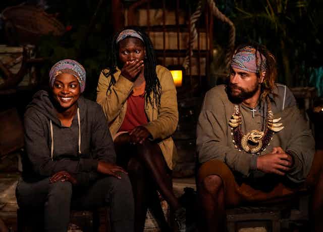 Three people sit during a tribal council