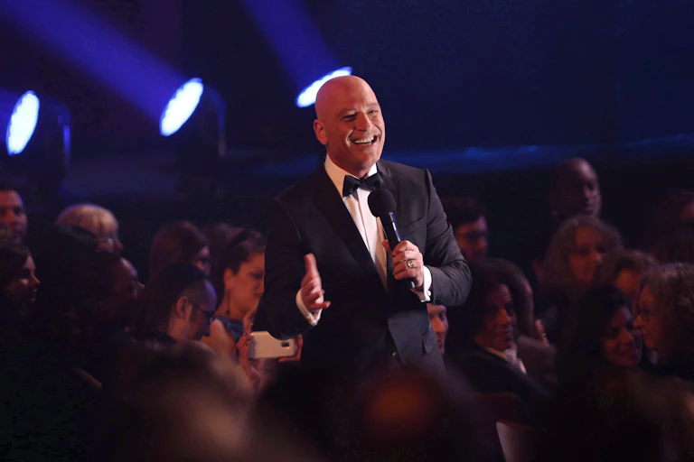 A man delivers stand-up comedy wearing a suit to a crowd