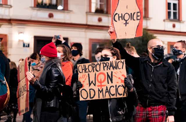 Men and women dressed in black and red holding handmade signs with Polish slogans and illustrations of women's bodies and the word CHOICE across the stomach.