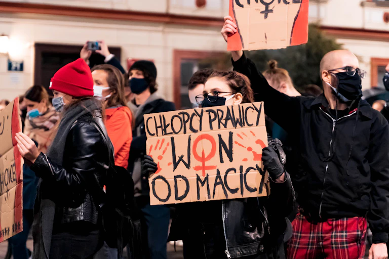 Men and women dressed in black and red holding handmade signs with Polish slogans and illustrations of women's bodies and the word CHOICE across the stomach.
