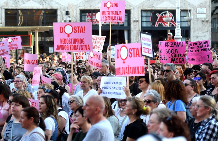 A crowd of people with pink placards with Croatian language slogans related to abortion rights