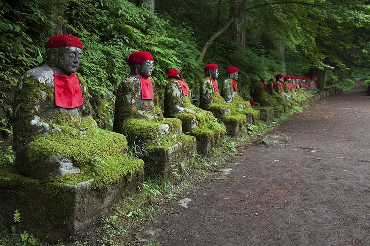 A row of small mossy statues of seated figures along a path in the forest.