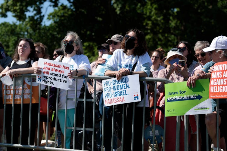 A line of protesters hold signs behind a fence.