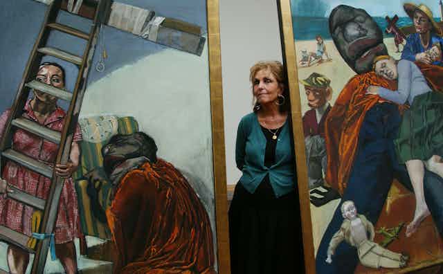 Paul Rego standing between two of her paintings.
