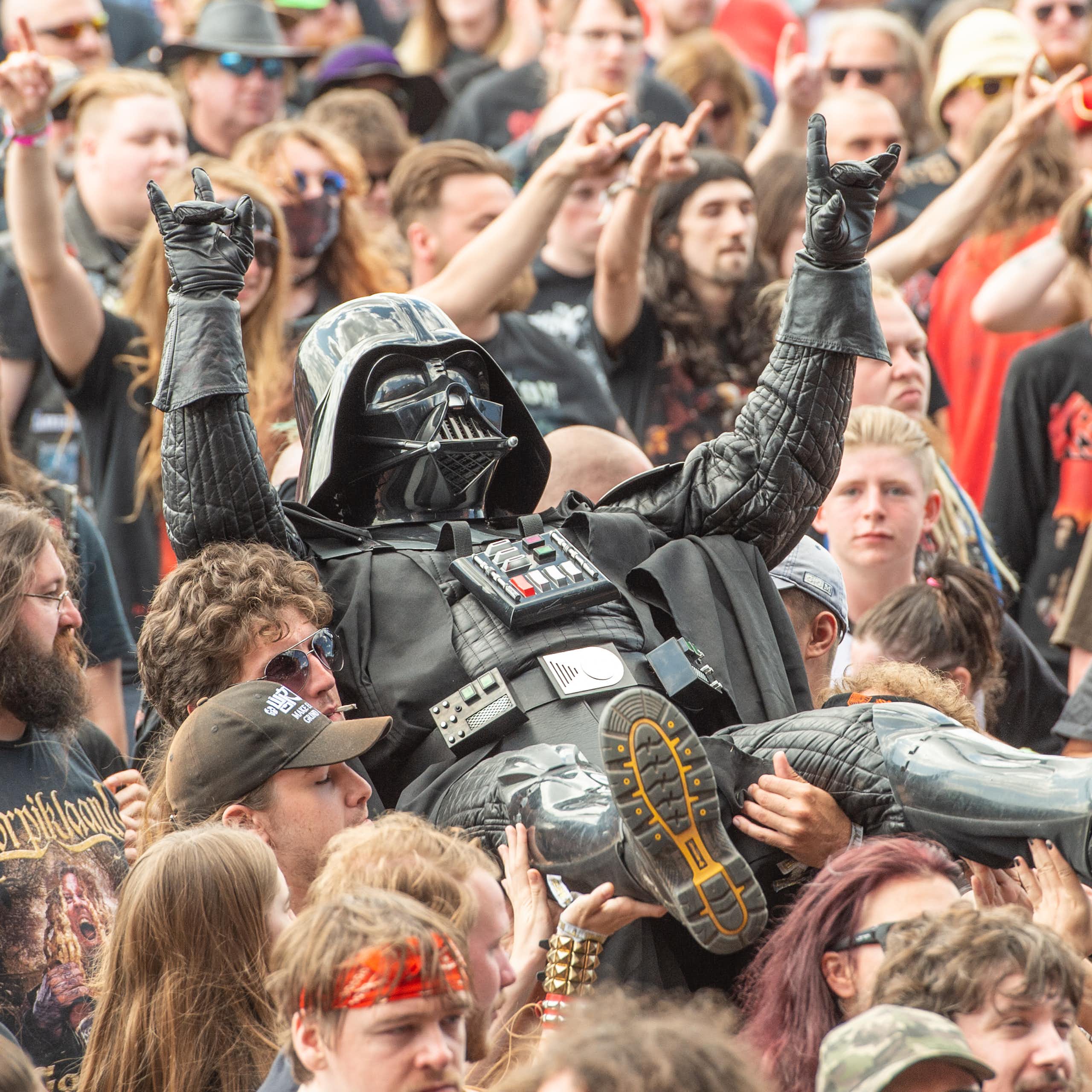 A person in a Darth Vader costume flashes a heavy metal salute as he is carried by others in the crowd.