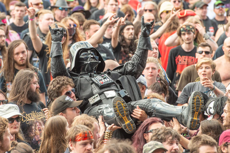 A person in a Darth Vader costume flashes a heavy metal salute as he is carried by others in the crowd.