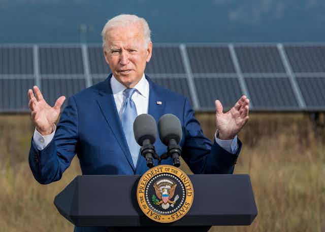 Biden speaks at a podium with a solar panel behind him