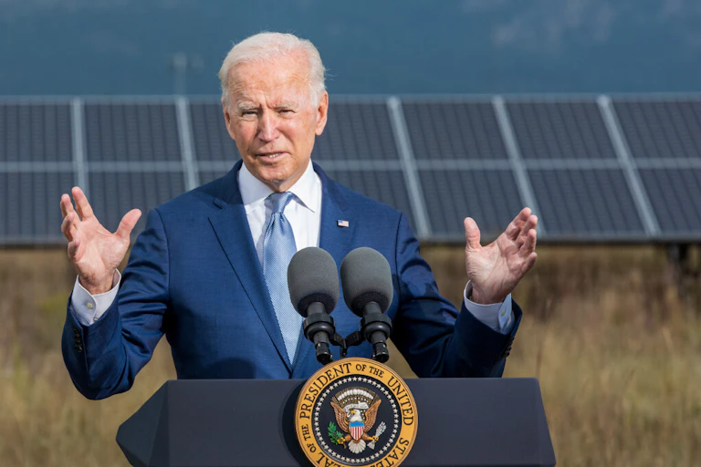 Biden speaks at a podium with a solar panel behind him