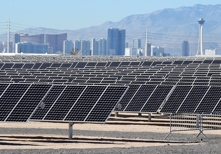 A field of solar panels in the desert with Las Vegas casinos and mountains in the background.