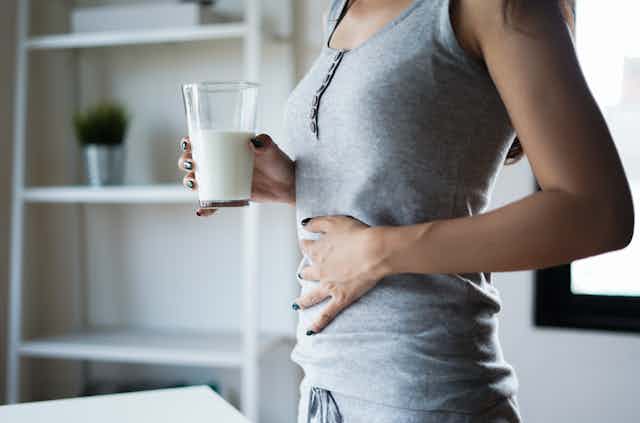 Woman clutching her stomach and holding glass of milk