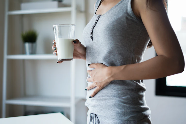 Woman clutching her stomach and holding glass of milk