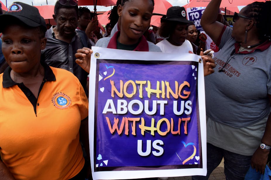 Women protesting, one holding a poster that reads, 'Nothing about us without us.'