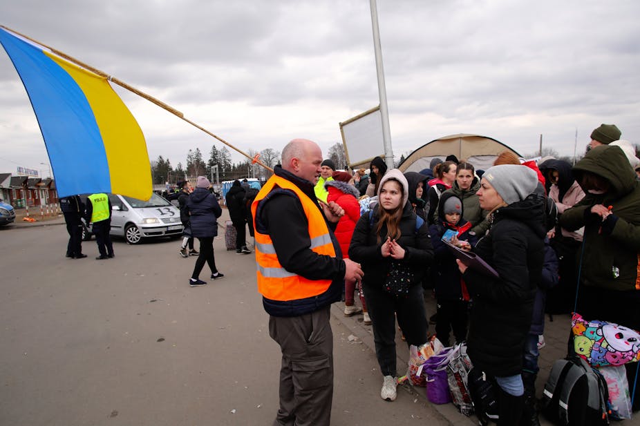 Volontaire tenant un drapeau ukrainien devant une foule de réfugiés.