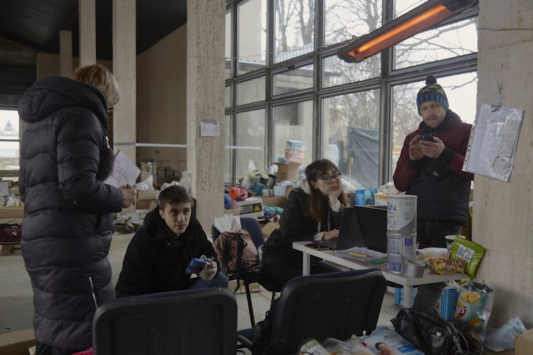 People use computers and smartphones amid piles of supplies in a mostly empty building