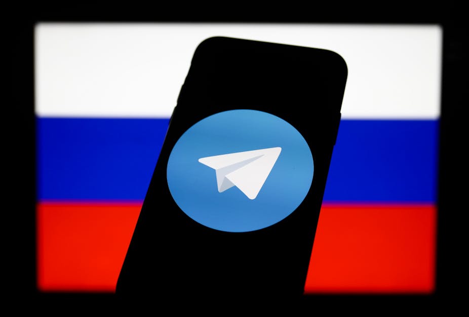 A smartphone displays the Telegram app logo in front of a Russian flag