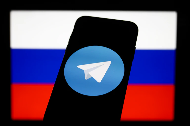 A smartphone displays the Telegram app logo in front of a Russian flag