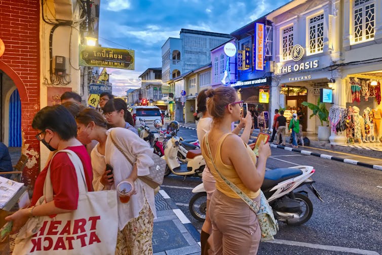 Tourists outside a restaurant on a Thai street in the evening.