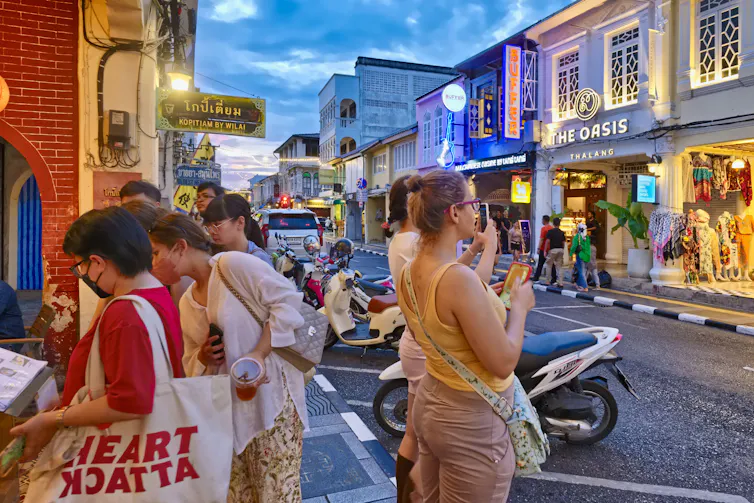 Tourists outside a restaurant on a Thai street in the evening.