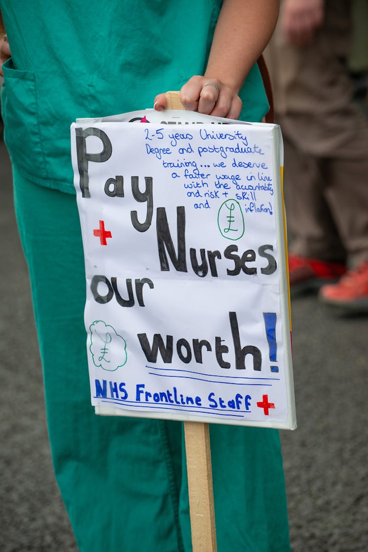 A nurse in green scrubs holds up a poster demanding better pay.