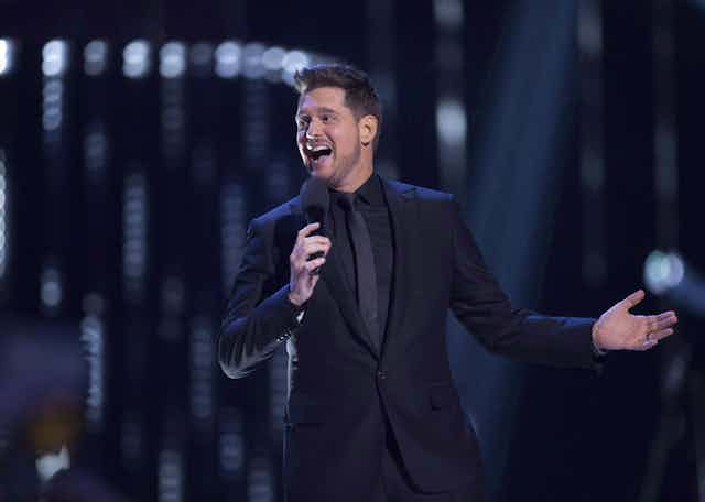 Singer Michael Bublé singing with a microphone in his hand, wearing a black suit