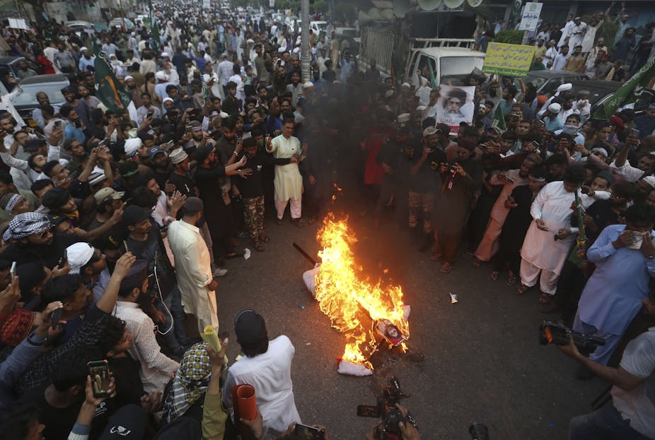 A large crowd gathers around a burning effigy during a demonstration.