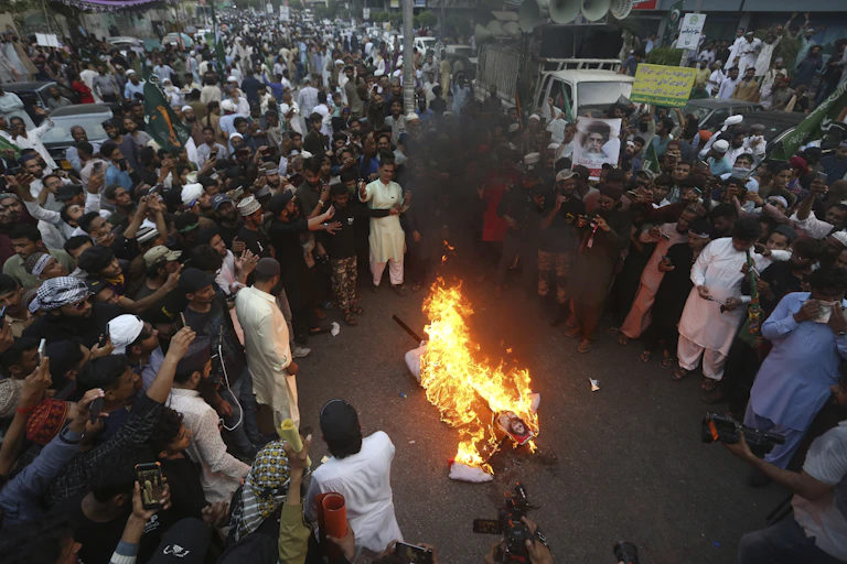A large crowd gathers around a burning effigy during a demonstration.
