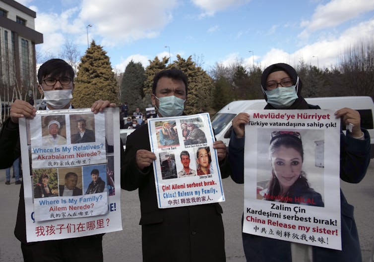 Two men and one woman holding posters with photographs of missing Uyghurs.