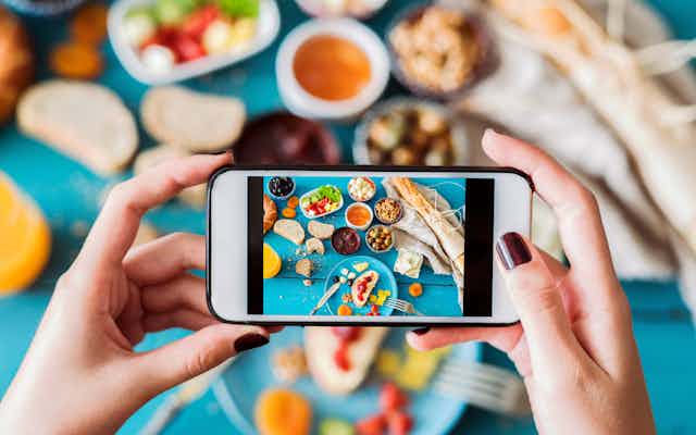 Cellphone taking a photo of food spread on top of a blue tablecloth