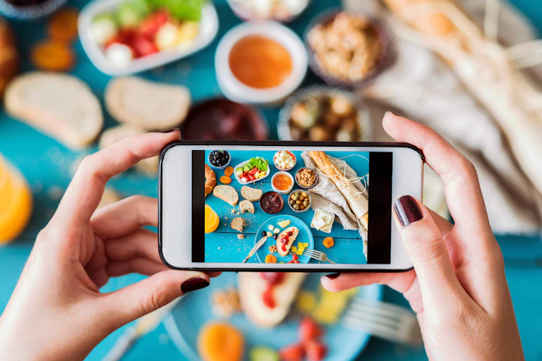 Cellphone taking a photo of food spread on top of a blue tablecloth