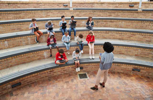 A teacher stands in front of students in an outdoor amphitheater