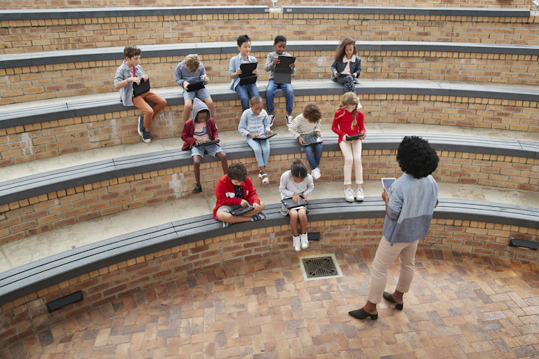 A teacher stands in front of students in an outdoor amphitheater
