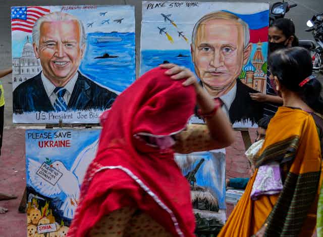Une femme en sari rouge passe devant des illustrations montrant Biden et Poutine