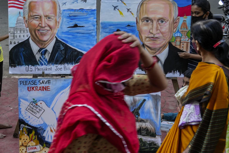 Une femme en sari rouge passe devant des illustrations montrant Biden et Poutine