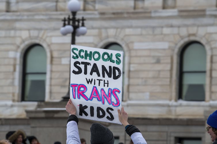 A person holds a sign that reads 'Schools Stand with Trans Kids'