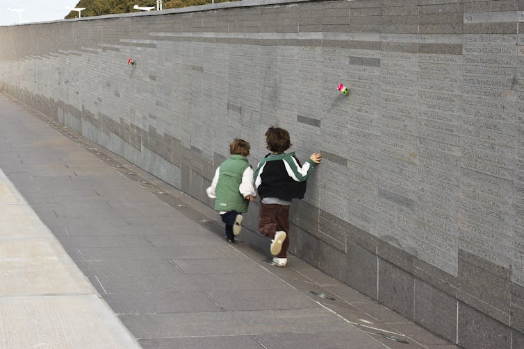Two small children touch a long wall on which thousands of names are inscribed.