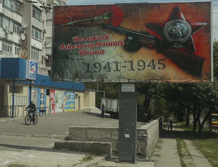 A man riding a bicycle past a poster reading 'Great Patriotic War 1941-1945', in Kherson, Ukraine, May 2022.