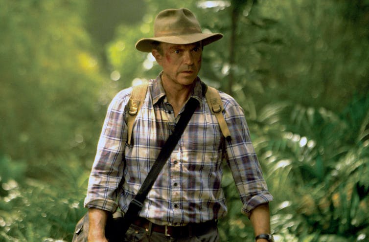 Alan Grant wears a lumberjack shirt and wide-brimmed hat