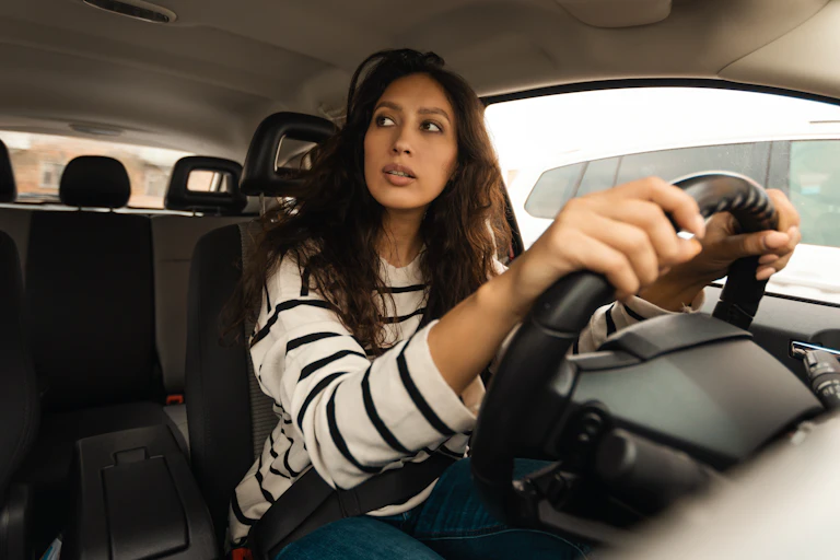 a woman behind the wheel of a parked car and looking out of the window