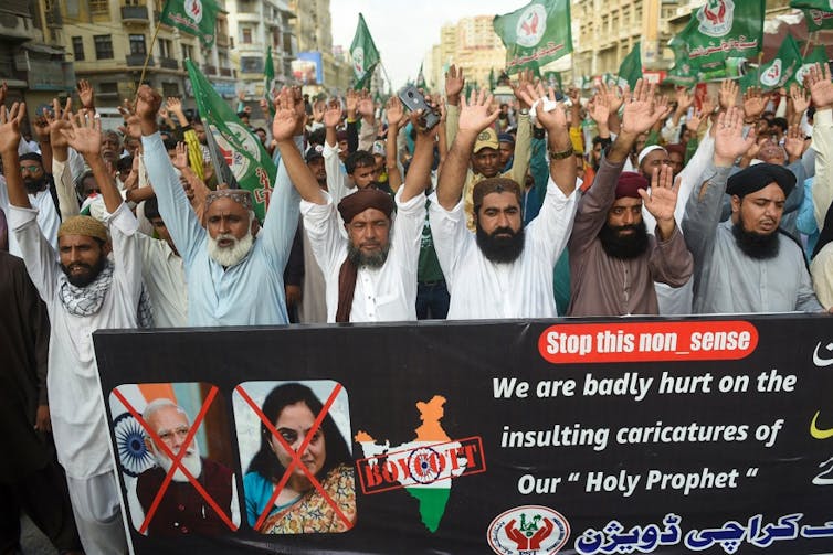 Des hommes manifestent devant une banderole proclamant « Nous sommes profondément blessés par les caricatures insultantes de notre Saint Prophète »