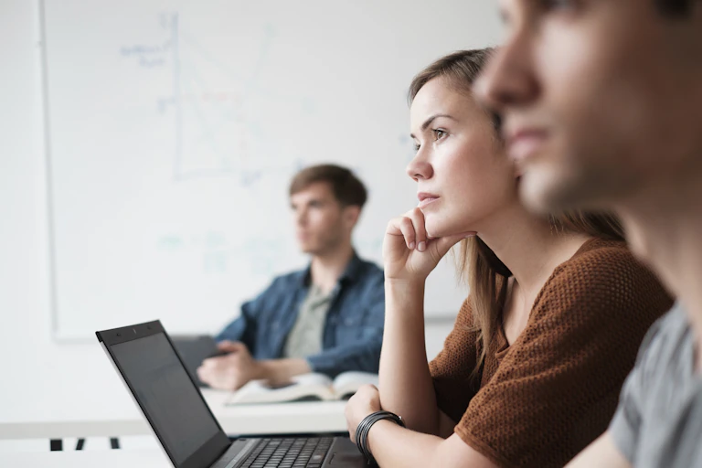 Three adult students – a woman and two men – look to the front of the class.