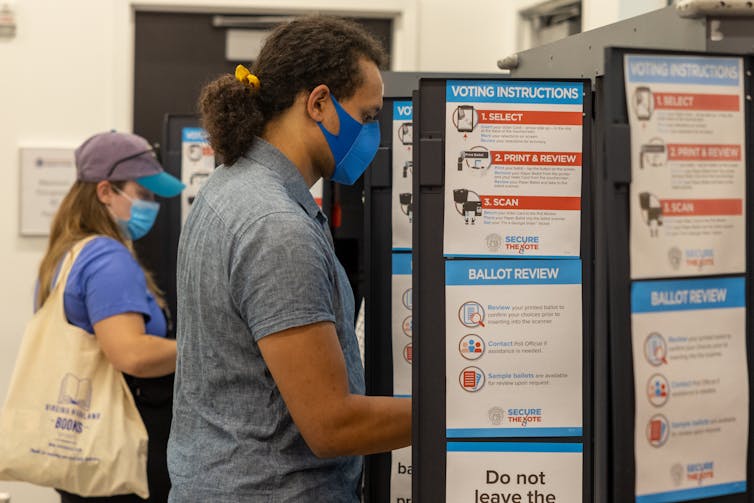 Two people, a man and a woman, voting at booths with a lot of writing on them.