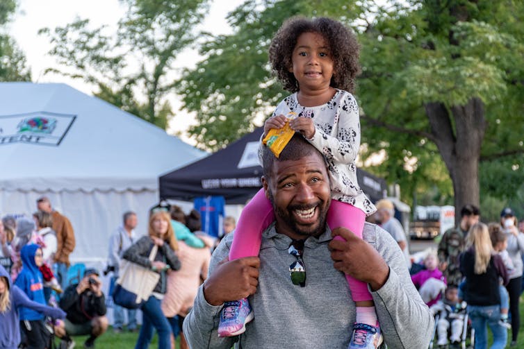 A little girl is seen sitting on her father's shoulders.