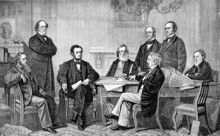 Seven white men gather around a table to watch President Abraham Lincoln sign the Emancipation Proclamation.