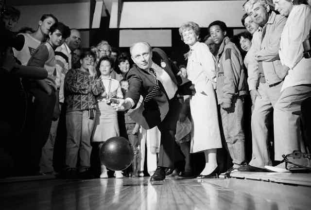 Neil Kinnock bowling while members of the public watch. 